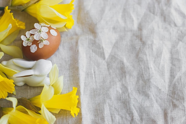 Fröhliche Ostern Ostereier geschmückt mit Blumen auf rustikalem Leinen mit Narzissen und Hasen