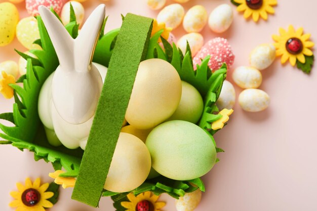 Fröhliche Ostern Ostereier und Kaninchen im grünen Korb auf rosa Hintergrund mit weißen und gelben Rosen Frühling Fröhliche Osterfeiertagskarte Osterhintergrund mit Kopierbereich Ansicht von oben