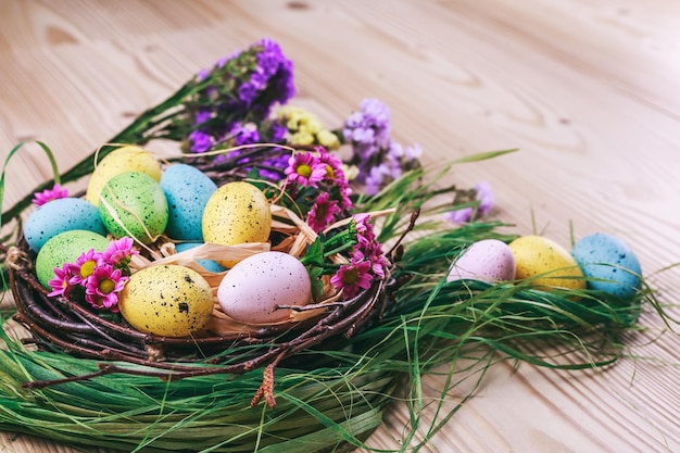 Fröhliche Ostern Osterhintergrund helle bunte Eier im Nest mit Frühlingsblumen über dunklem Holzbac