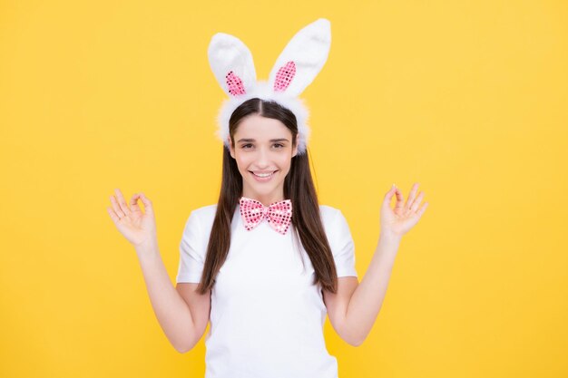 Fröhliche Ostern Porträt einer jungen lächelnden Frau mit Hasenohren isoliert auf gelbem Studiohintergrund Osterhasenfrau sieht lustig aus Kaninchenmädchen zeigt auf Kopierraum