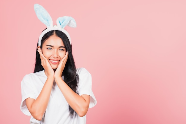 Fröhliche Ostern. Schöne junge Frau Teenager lächelnd tragen Osterhasen Hasenohren hält ihre Wangen aufgeregt überrascht, Portrait weibliche Gesichts-Touch-Massage, Studioaufnahme isoliert auf rosa Hintergrund