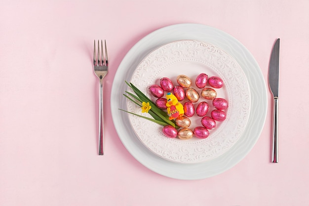 Fröhliche Ostern Tischdekoration für Osterferien Ostereier Entenblume und Besteck auf rosa Hintergrund Draufsicht flach gelegt