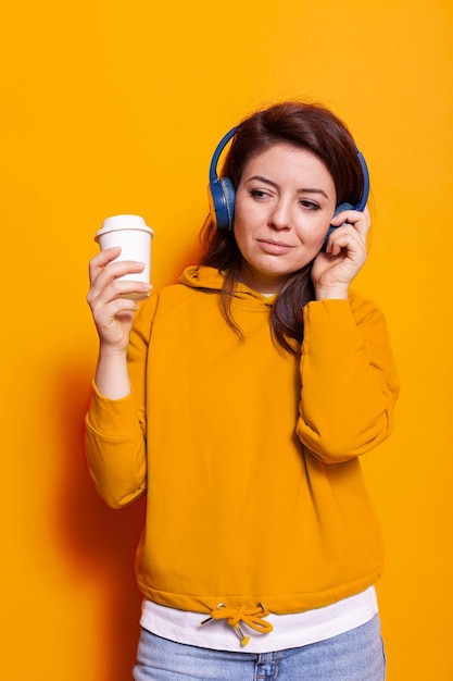 Fröhliche Person mit einer Tasse Kaffee, die Musik über Kopfhörer hört. Kaukasische Frau, die sich entspannt fühlt und das Lied auf dem Headset genießt, während sie ein heißes Getränk zum Trinken hält. Junger Erwachsener entspannt