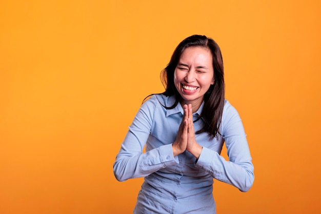 Fröhliche philippinische Frau, die zu Gott betet und um Vergebung bittet, posiert mit zusammengelegten Handflächen im Studio vor gelbem Hintergrund. Positiver hoffnungsvoller junger Erwachsener, der religiöse spirituelle Geste zeigt