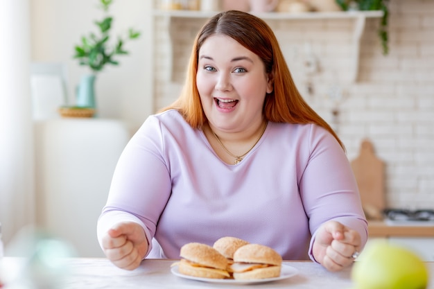 Fröhliche positive Frau, die vor Burgern sitzt, während sie sie essen möchte