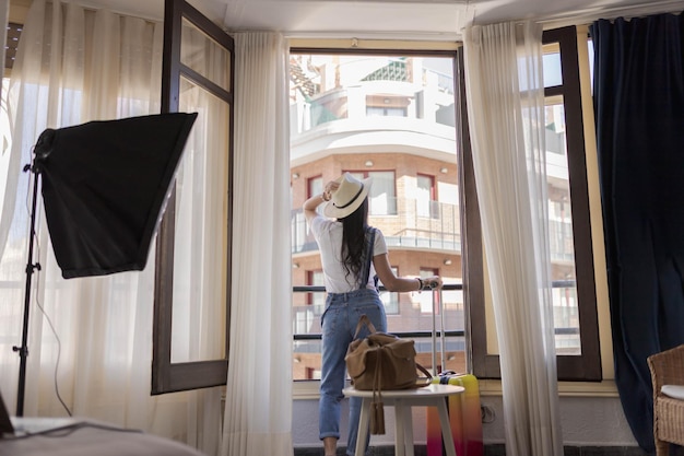 Fröhliche, reiche junge Frau, die einen Nachtmantel trägt, steht am großen Fenster, offene Spitzenvorhänge im Schlafzimmer, Blick nach draußen, genießen Sie die Aussicht, träumen Sie, fühlen Sie sich motiviert im modernen Heimhotel, Guten Morgen, Lifestyle-Konzept, Rückansicht