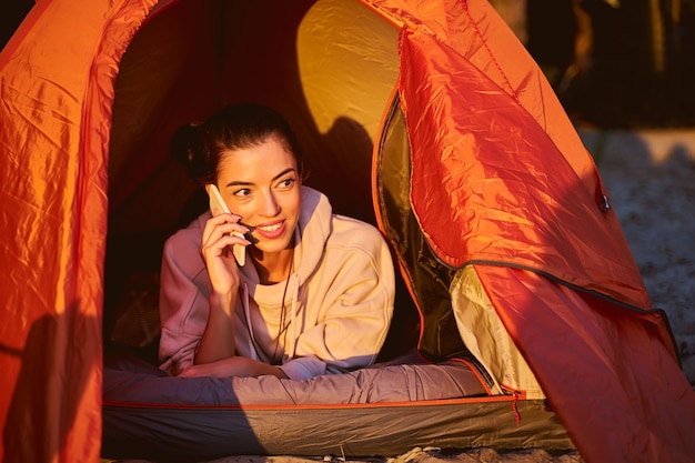 Fröhliche Reisende, die Telefongespräche führen und lächeln, während sie sich im touristischen Zelt ausruhen?