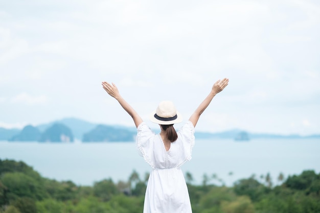 Fröhliche Reisende Frau in weißem Kleid genießen Schöne Aussicht allein Tourist mit Hut, der über Ozeanreise-Sommer- und Urlaubskonzept steht und sich entspannt