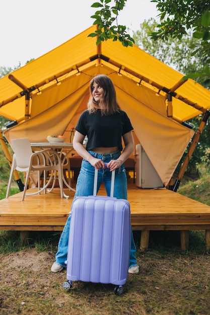Fröhliche Reisende mit Gepäck, die auf dem Hintergrund eines gemütlichen Glamping-Hauses stehen Luxus-Campingzelt für Sommerferien und Urlaub im Freien Lifestyle-Konzept