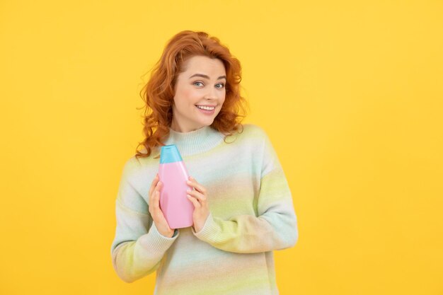 Fröhliche rothaarige Frau mit lockigem Haar, die Shampoo- oder Lotionsschönheit präsentiert