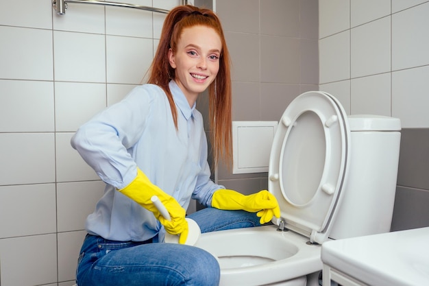 Fröhliche rothaarige Ingwerfrau, die sich in der Toilette mit Handschuhen in der Toilette wäscht.
