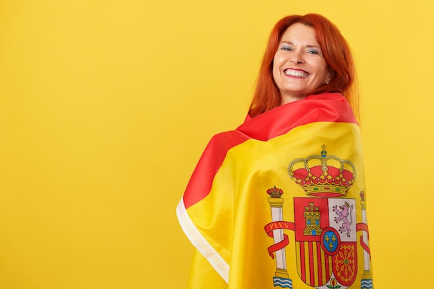 Foto fröhliche, rothaarige, reife frau, die sich mit einer spanischen nationalflagge umhüllt