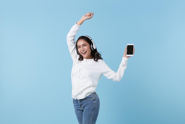 Fröhliche schöne asiatische Teenager-Frau, die Musik auf dem Handy hört, trägt Kopfhörer und tanzt