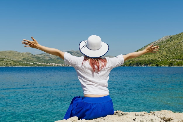 Fröhliche, schöne junge Frau, die die Freiheit und die Sommerferien mit Meerblick genießt