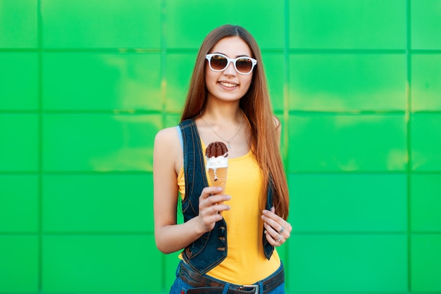 Fröhliche schöne junge Frau lächelnd, die ein Eis nahe der hellgrünen Wand hält