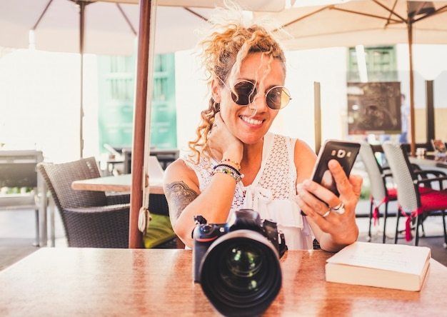 Foto fröhliche schöne junge frau lächelt und telefoniert mit moderner kamera vor ihr am tisch im restaurant