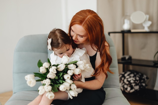 Foto fröhliche, schöne, liebevolle mutter mit einem strauß frühlingsblumen umarmt ihre tochter zu hause auf dem bett und genießt den moment der überraschung, der den muttertag feiert