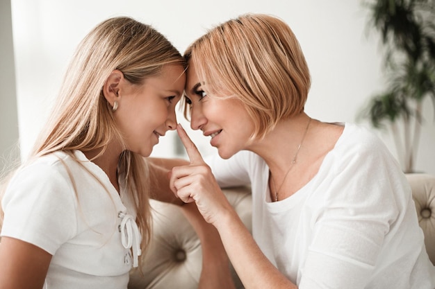 Fröhliche, schöne Mutter und Tochter, die Zeit miteinander verbringen, sich umarmen und Spaß haben, während sie zu Hause auf der Couch sitzen. Familienkonzept