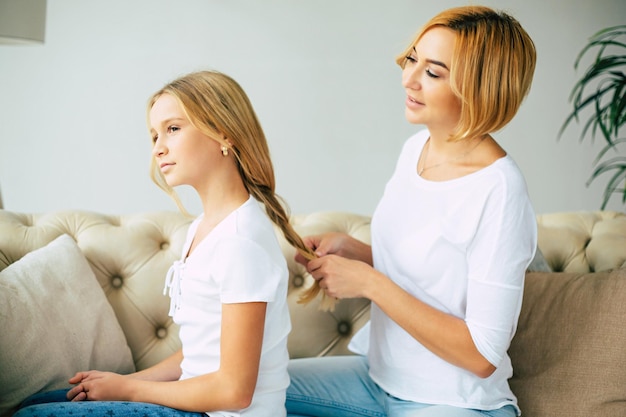 Fröhliche, schöne Mutter und Tochter, die Zeit miteinander verbringen, sich umarmen und Spaß haben, während sie zu Hause auf der Couch sitzen. Familienkonzept