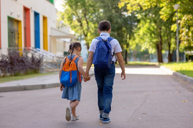 Fröhliche Schulkinder, ein kleines Mädchen und ein Junge in einem weißen Hemd mit Rucksäcken