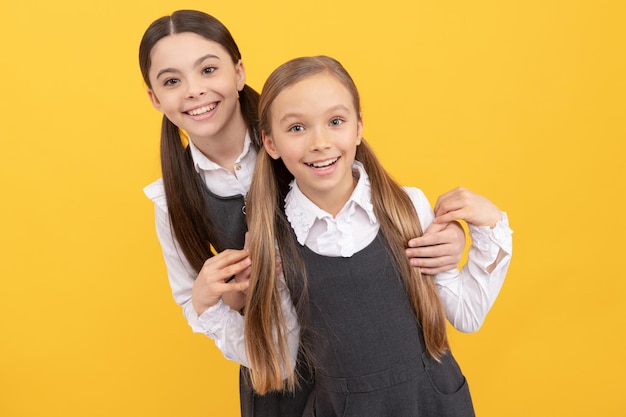 Fröhliche Schulkinder mit Beauty-Look tragen lange Haare im Salon mit gelbem Hintergrund in formellen Uniformen