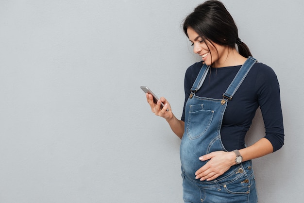 Fröhliche schwangere Frau, die durch Handy plaudert