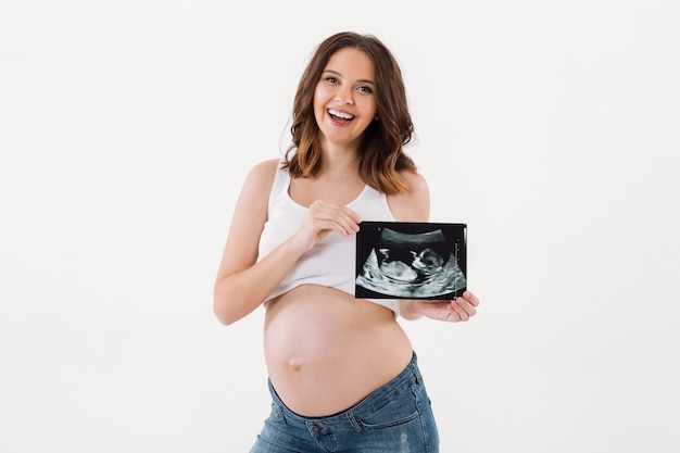 Fröhliche schwangere Frau, die Ultraschallabtastung eines Babys hält.