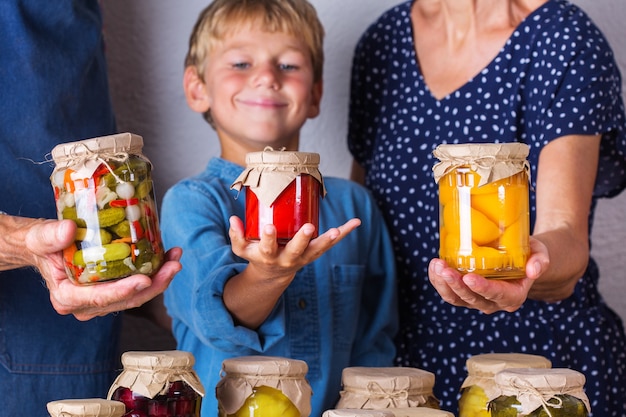 Fröhliche Senioren, Großmutter, Großvater und kleiner Junge, Enkel, der Gläser mit hausgemachten konservierten und fermentierten Lebensmitteln in den Händen hält, eingelegt und mariniert. Ernteerhalt, Familienzeit