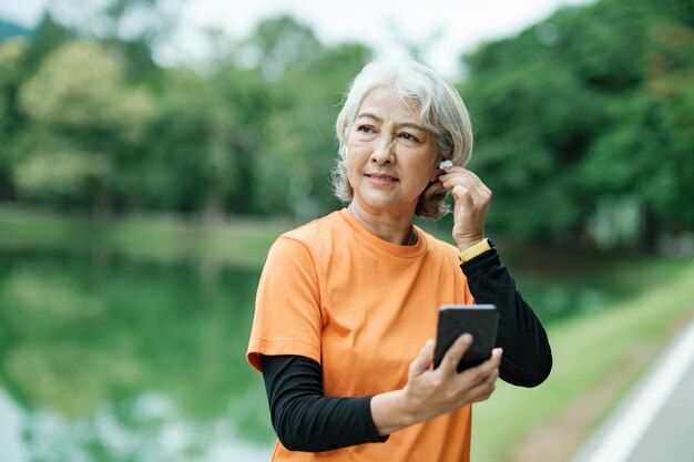 Fröhliche sportliche Seniorin, die Musik auf dem Handy hört und ihre Smartwatch überprüft.