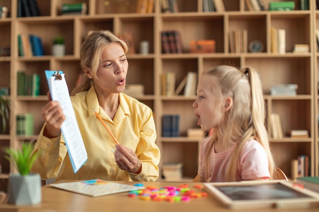 Foto fröhliche sprachtherapeutin, die mädchen39s probleme und hindernisse heilt, süßes kind lernt und spricht buchstaben aus