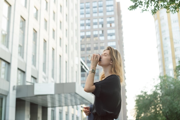 Fröhliche, stilvolle Geschäftsfrau, die draußen Kaffee trinkt, auf urbanem Hintergrund