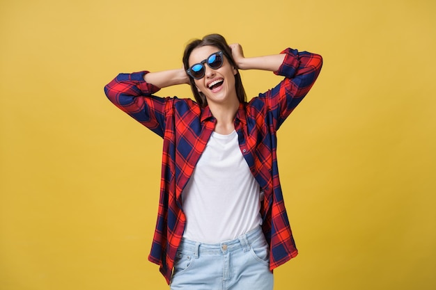 Fröhliche, stilvolle, moderne Frau mit modern geformter Sonnenbrille, die lachend auf Ihre Kamera schaut, die auf gelbem Hintergrund isoliert ist Glückskonzept