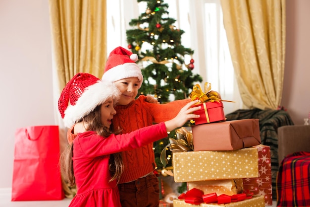 Fröhliche süße Kinder, die Weihnachtsgeschenke nehmen. Glückliche Familienfeier Heiligabend zu Hause