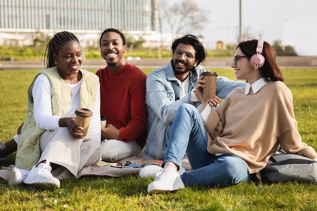 Fröhliche tausendjährige multiethnische moderne Studenten mit einer Tasse Kaffee zum Mitnehmen lernen gemeinsam, sich auszuruhen
