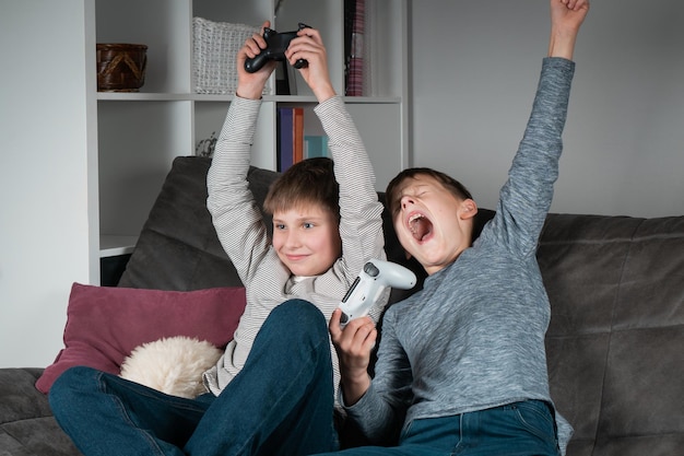 Fröhliche Teenager sitzen mit erhobenen Armen und Spiel-Joysticks auf dem Sofa Fröhliche Jungs spielen Videospiele Lebensstil der besten Freunde