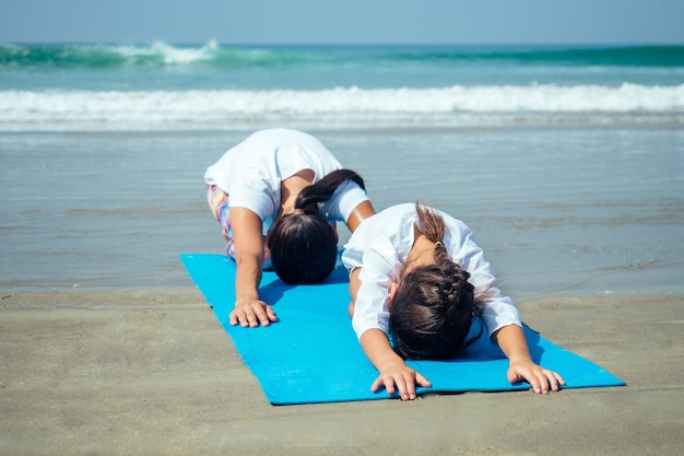 Fröhliche Tochter und Mutter beim Yoga am Strand