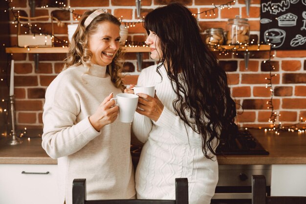 Fröhliche und fröhliche Frauen, die zu Hause in der Küche Kaffee sprechen und trinken. Blondine und Brünette reden miteinander