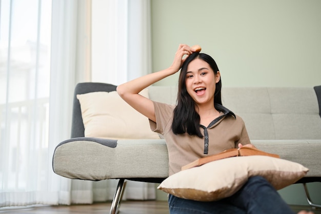 Fröhliche und glückliche asiatische Frau in ihrem Wohnzimmer, die ein Buch liest und nascht