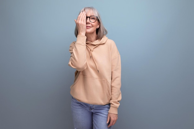 Fröhliche, verträumte, modische, reife Frau im Jugendoutfit, die auf Studiohintergrund mit Kopie flirtet