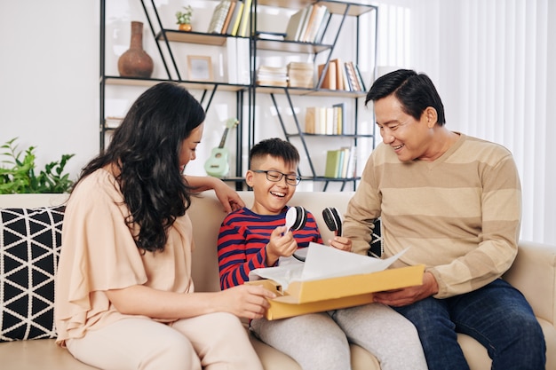 Fröhliche vietnamesische Eltern geben Sohn große Box mit modernen Kopfhörern zum Geburtstag