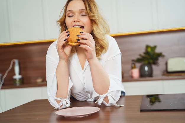 Fröhliche weibliche Person, die die Augen geschlossen hält, während sie leckeren Burger beißt