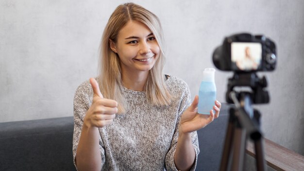 Fröhliche weibliche Schönheitsblogger, die Video zu Hause aufzeichnet. Sie zeigt Lotion für die Haut und ein Zeichen wie von Hand