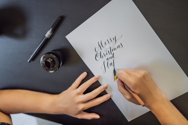 Fröhliche Weihnachten. Kalligraph junge Frau schreibt Satz auf weißem Papier