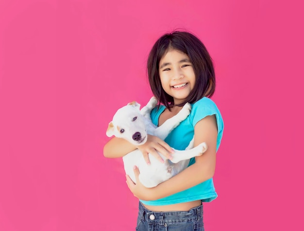 Fröhliche Welpen und asiatische Kinder in Liebe umarmen sich auf rosafarbenem Hintergrund