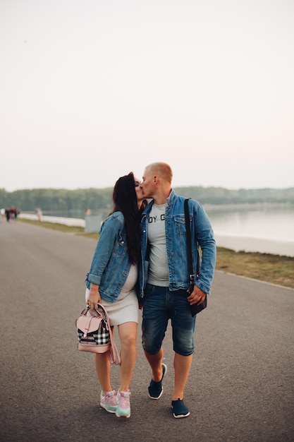 Fröhliche zukünftige Eltern, die zusammen an der frischen Luft spazieren gehen und einander anschauen und lachen Schwangere Frau mit Ehemann, die ein Baby erwartet, das sich entspannt und gemeinsam Freizeit verbringt Konzept der Schwangerschaft