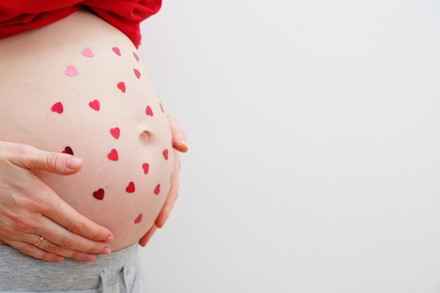Fröhlichen Valentinstag. Eine schwangere Frau mit herzförmigen Pailletten auf ihrem Bauch. Das Konzept der Mutterschaft. Babydusche