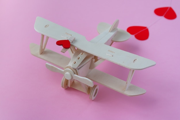 Fröhlichen Valentinstag. hölzerne Kinderflugzeug auf einer rosa Oberfläche mit rotem Herzen und Girlande in Form eines Herzens