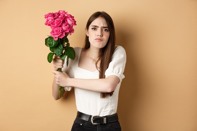 Fröhlichen Valentinstag. Wütendes Mädchen, das jemanden mit Blumen schlägt und Rosenstrauß an Freund schwingt