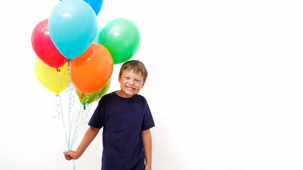 Fröhlicher achtjähriger Junge mit einem Arm voller leuchtend bunter Luftballons feiert Geburtstag