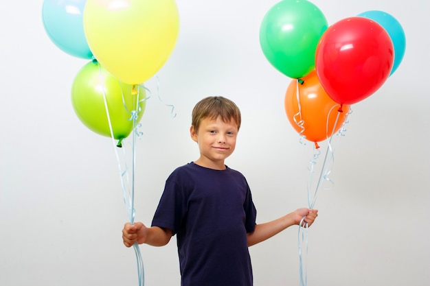 Fröhlicher achtjähriger Junge mit einem Arm voller leuchtend bunter Luftballons feiert Geburtstag